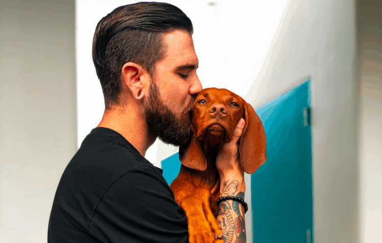 Man with well trimmed beard kissing dog