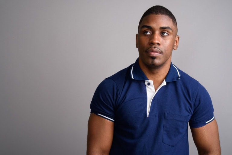 A man wearing a navy blue polo shirt stands against a plain gray background, looking slightly to his left with a neutral expression.