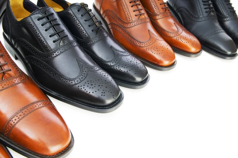 A row of polished mens leather dress shoes in brown and black, featuring different styles and decorative brogue patterns, arranged neatly on a white background.
