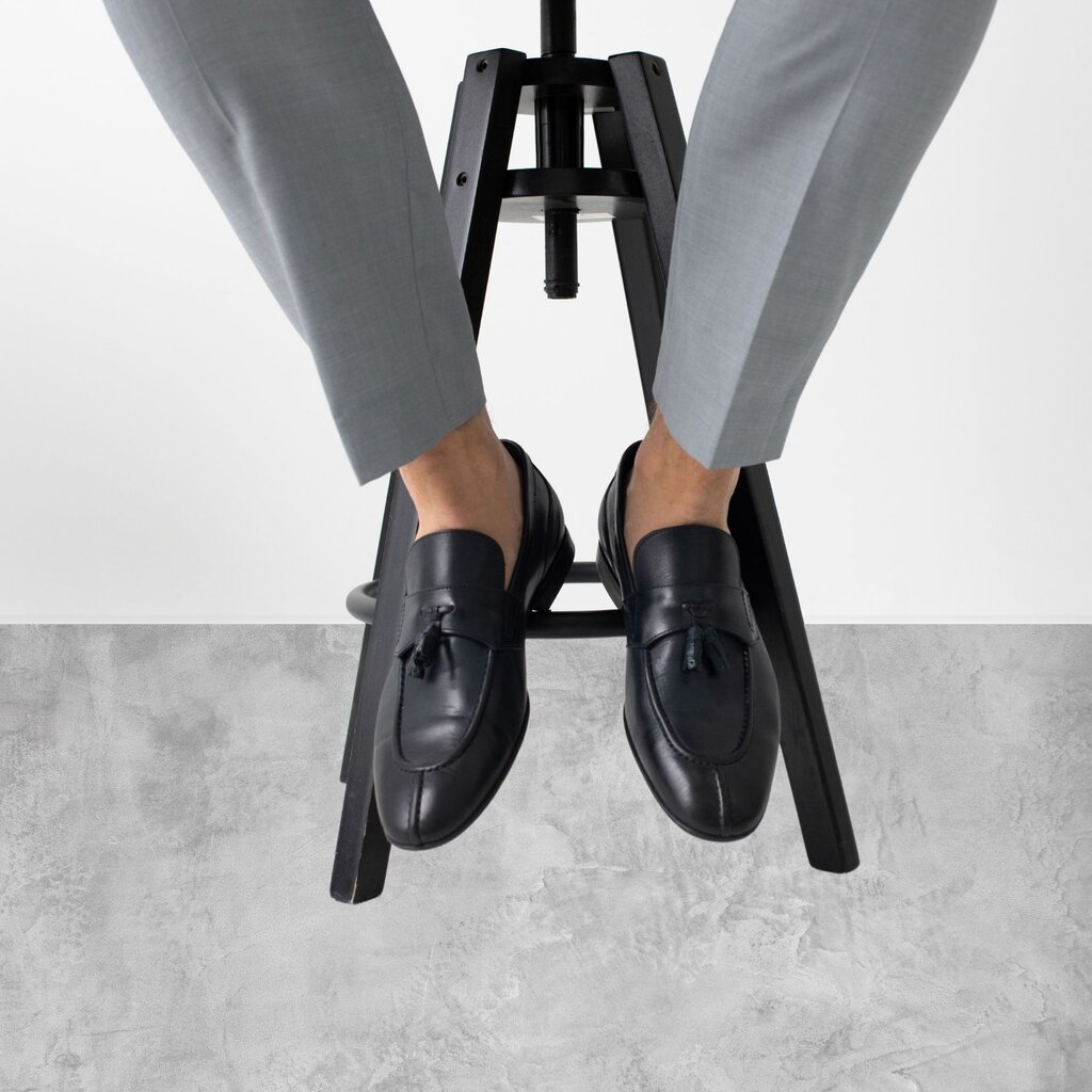 A persons legs in grey pants and black shoes.