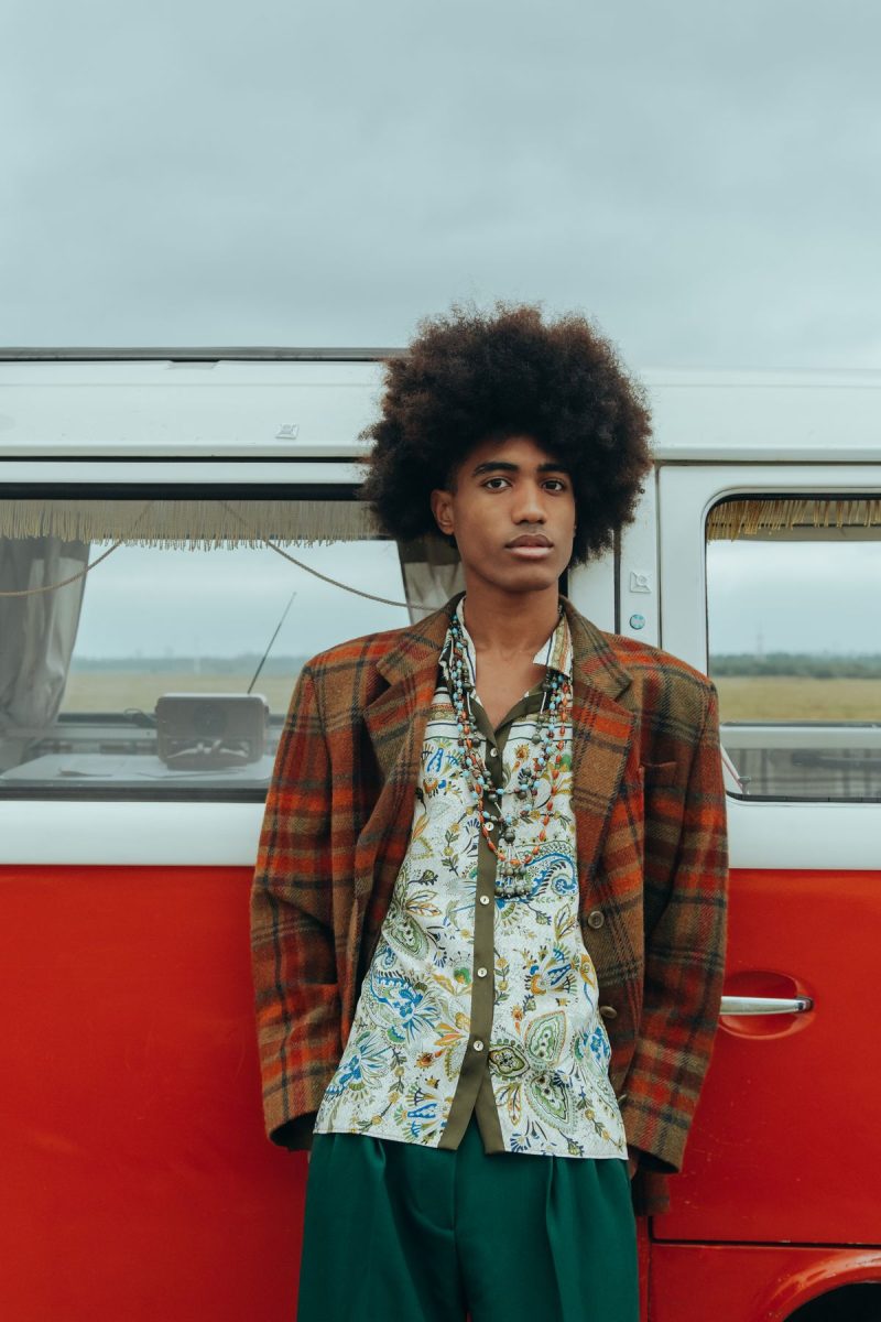 Man with an afro wearing a plaid blazer leaning against a classic van
