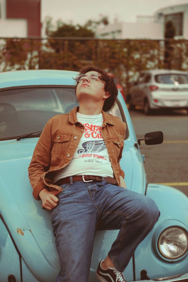 Man in a 70s-inspired outfit lounging on a vintage blue car