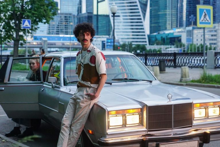 Man in retro 80s style leaning on a vintage car