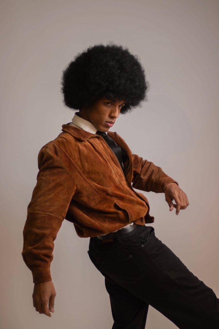Man with an afro wearing a brown suede 70s jacket