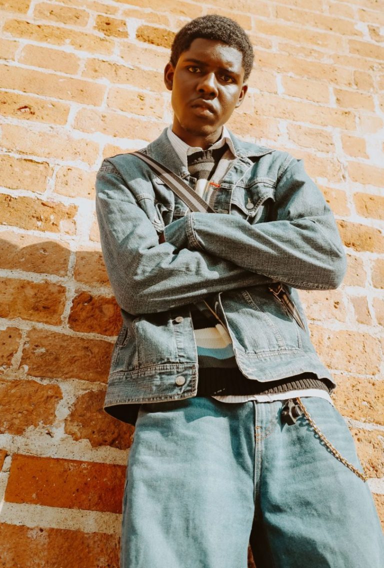 Young man in a denim jacket with 90s attitude against a wall