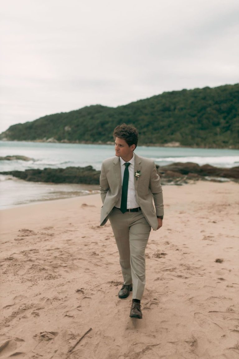 Man in a beige suit walking along a sandy beach