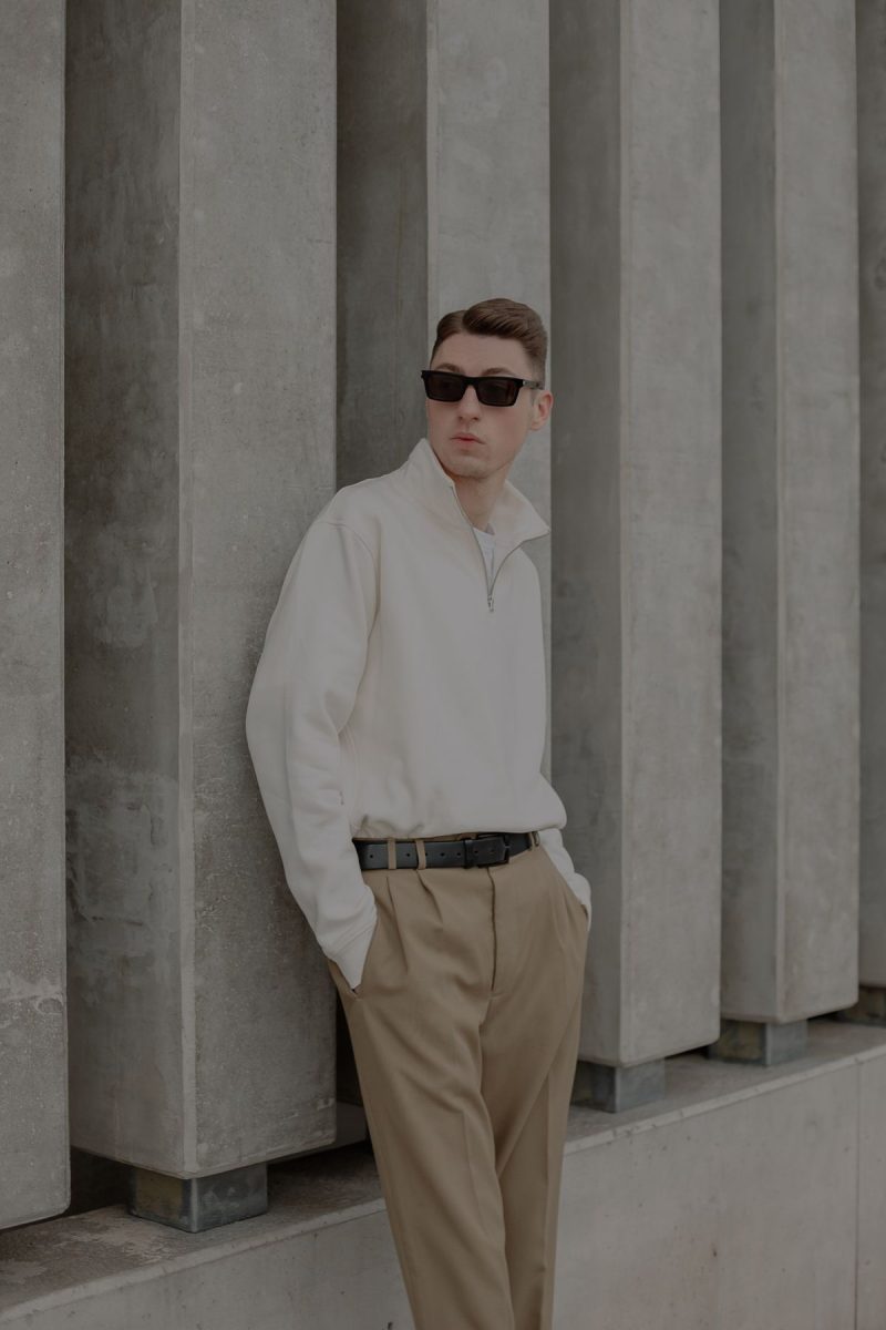 Man in a white shirt and tan trousers leaning against a concrete wall