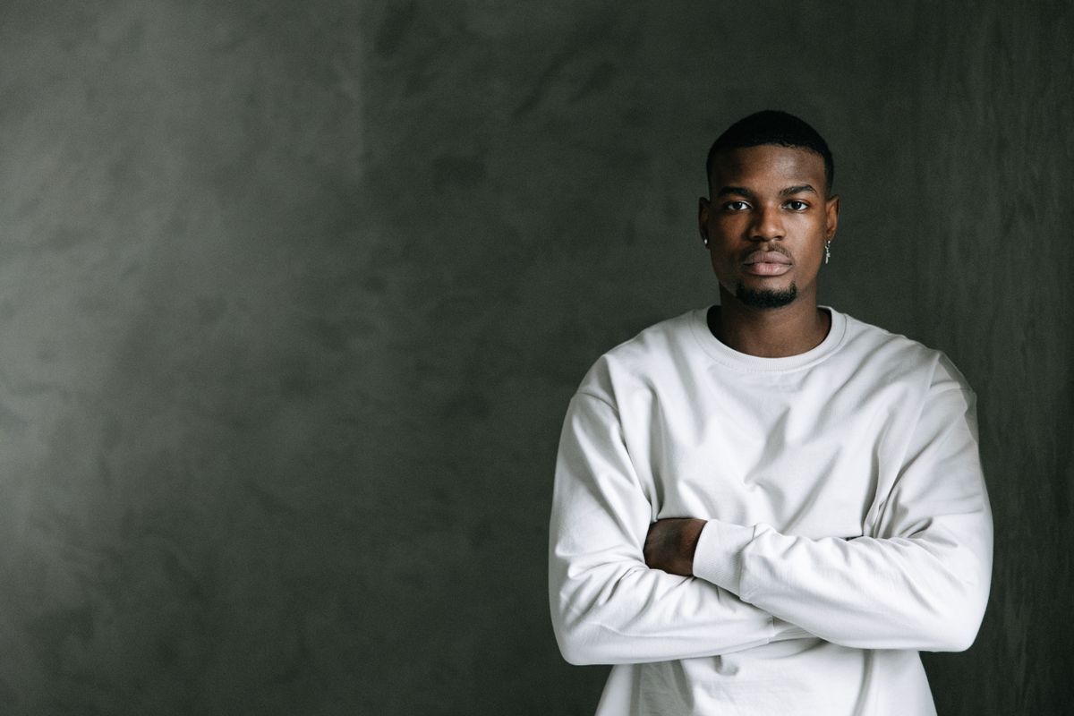Man in a plain white shirt with crossed arms against a grey backdrop