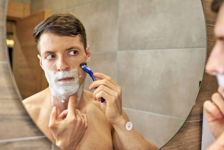 Man shaving with a razor at the bathroom mirror
