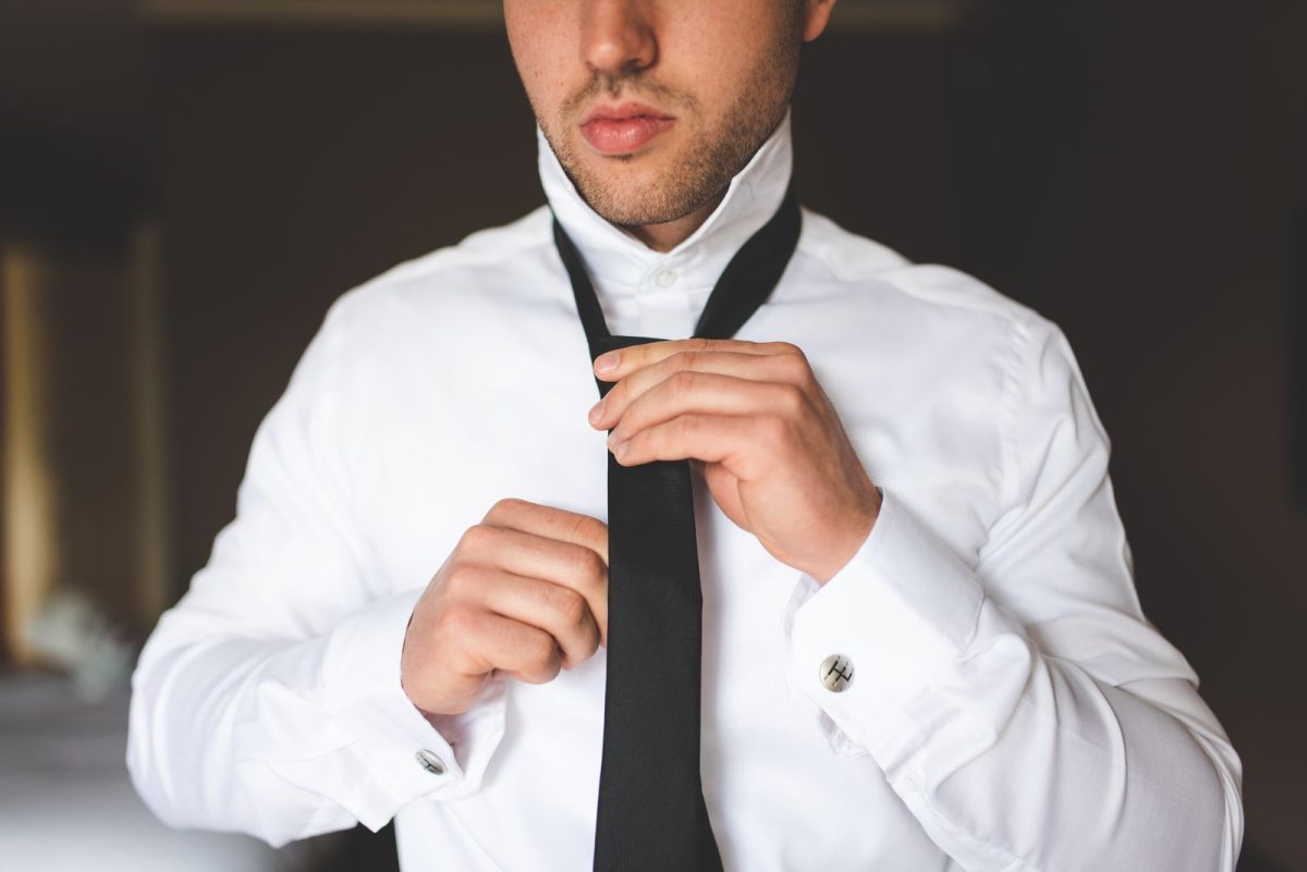 Close crop of hands knotting a black bow tie, cufflink visible