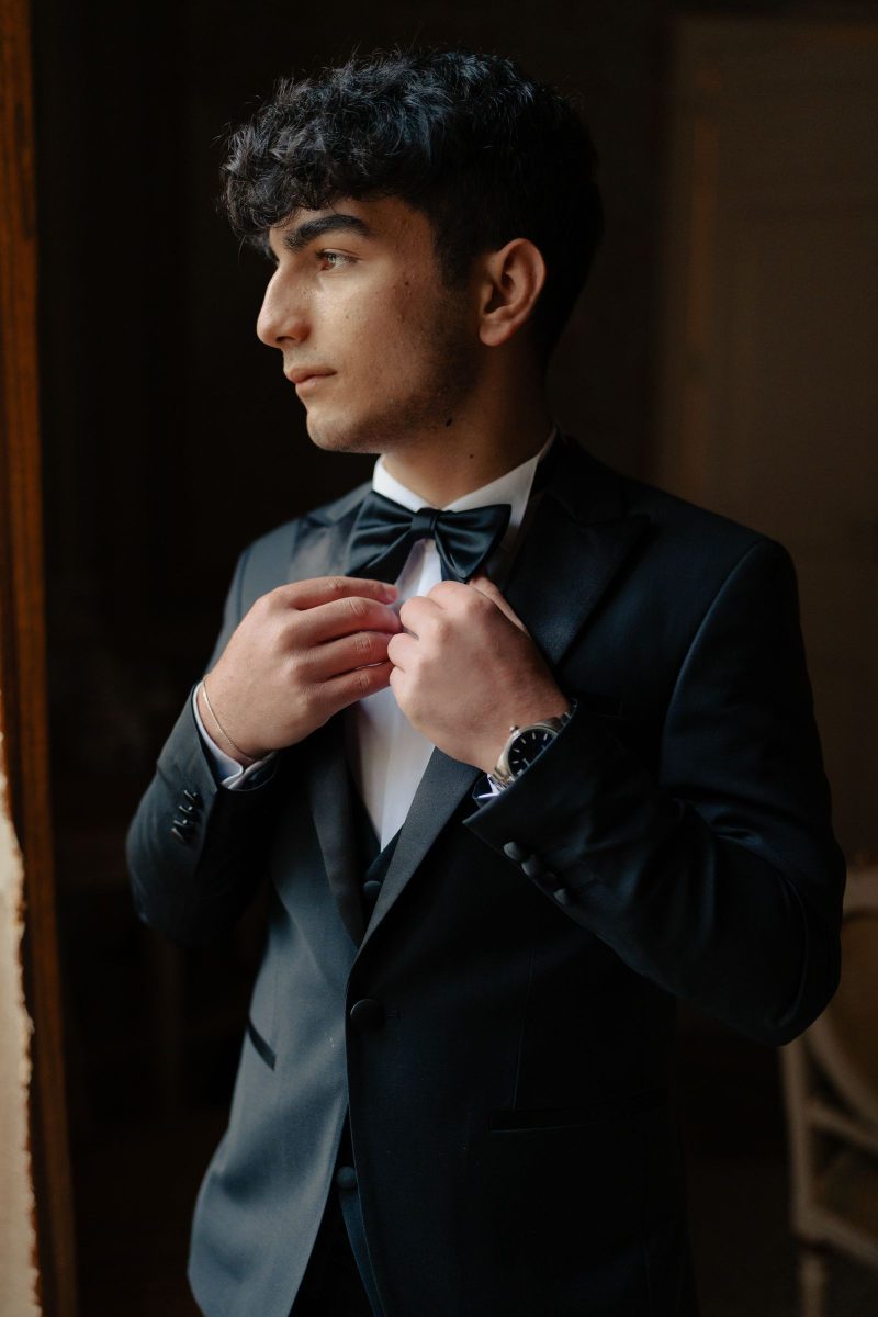 Low-key portrait of a man in a black tuxedo adjusting his bow tie