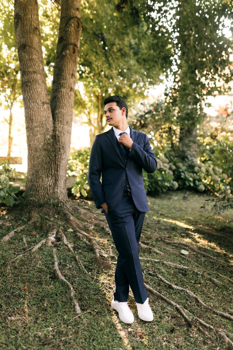 Man in a dark suit standing under trees in dappled natural light