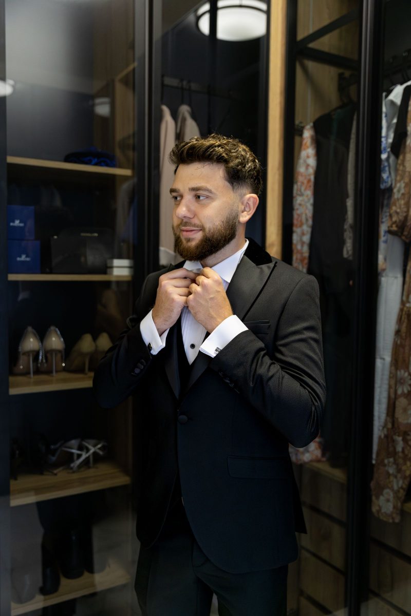 Man in a dinner jacket adjusting his lapel in a dressing room