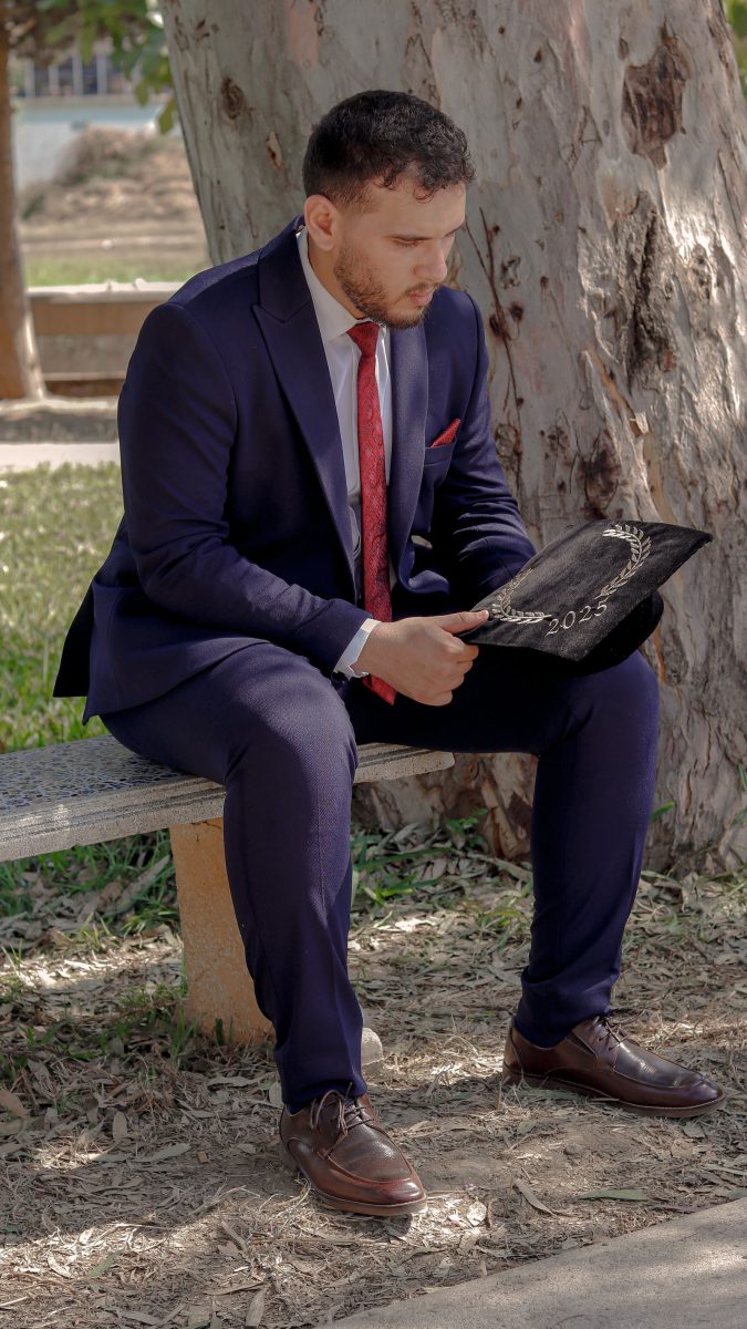 Graduate in a navy suit seated outdoors holding his cap