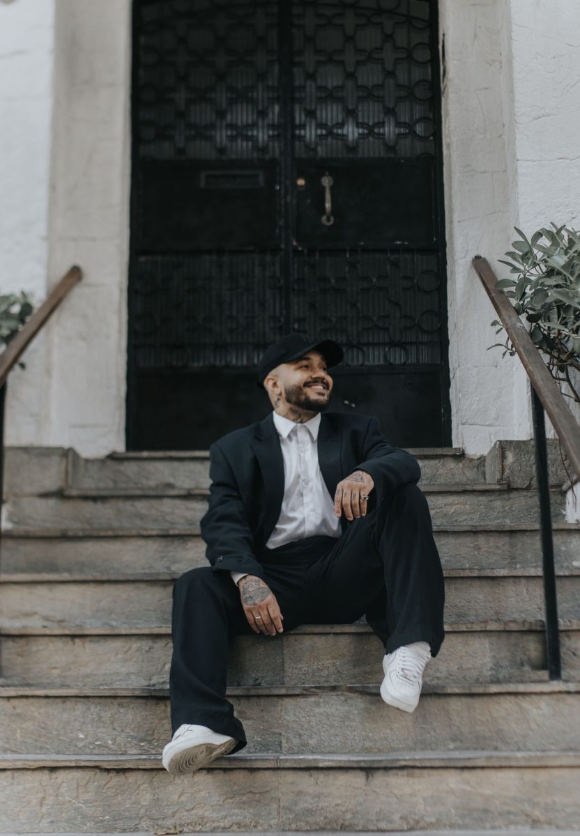 Man in a relaxed dark suit and sneakers seated on stone steps