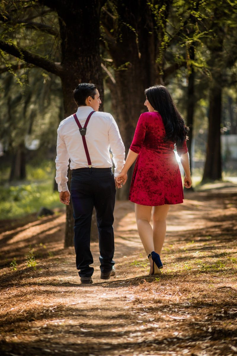 Couple walking down a tree-lined path, the man in braces and tailored trousers